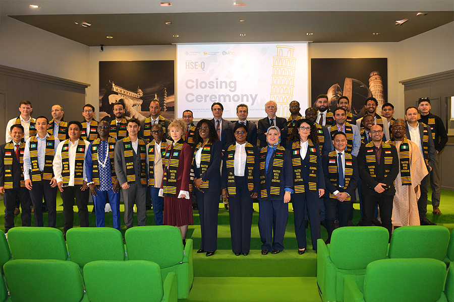 Un ampio gruppo di professionisti provenienti da diversi Paesi posa insieme durante la cerimonia conclusiva di un evento internazionale. I partecipanti, disposti su più file in una sala conferenze moderna, indossano stole decorative dai colori vivaci che richiamano tradizioni culturali differenti. Sullo sfondo, uno schermo proietta la scritta “Closing Ceremony” accanto all’immagine della Torre di Pisa, creando un’atmosfera celebrativa e istituzionale dedicata alla cooperazione e allo scambio multiculturale.